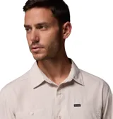 Camisa de manga larga Columbia, color beige, con cuello clásico, cierre frontal de botones y dos bolsillos en el pecho. Presenta un diseño técnico con ventilación en la espalda y mangas enrollables con broches de presión.