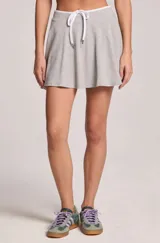 Pollera short corta de color gris melange, confeccionada en algodón. Presenta una silueta relajada y fluida con diseño acampanado y cintura elástica ajustable mediante cordón blanco.