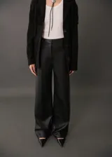 Pantalon de tiro medio con diseño wide leg y efecto cuero. Cuenta con trabillas para cinturón, cierre oculto de botón, gancho y cremallera, y dos bolsillos laterales de ribete.