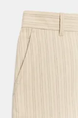 Pantalón barrel de tiro medio confeccionado en hilatura con lino, color beige con diseño a rayas sutiles. Cuenta con cintura con trabillas, bolsillos laterales ocultos en costura, pierna ancha y cierre frontal con cremallera y botón.