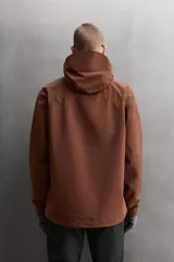 Cazadora deportiva color marrón confeccionada en tejido técnico de tres capas con membrana impermeable. Cuenta con cuello alto con capucha ajustable, mangas largas con puños reforzados ajustables, aberturas con cremallera en axilas, bolsillos frontales con cremallera y bajo ajustable con elásticos laterales.