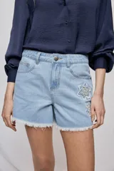 Short de denim blanco de calce recto y tiro medio, con bolsillos delanteros, cierre con botón y terminación desflecada en el ruedo. Presenta detalles florales bordados al tono en el frente.