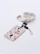 Tarjetero rectangular con estampado tipo terrazo en tonos beige, rosa, azul y negro. Incluye una cinta para el cuello a juego con estampado de puntos y un gancho metálico con cordón de seguridad.