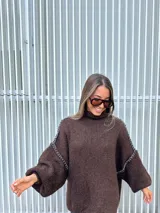 Buzo de punto oversize color chocolate, con cuello alto, mangas largas abullonadas y detalles de costuras bordadas a mano en color blanco en las uniones de las mangas.