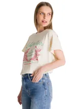 Remera de corte relajado color beige, con cuello redondo y mangas cortas. Presenta un estampado gráfico frontal con motivos botánicos y tipografía retro en tonos verde y rosado.