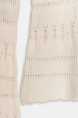 Jersey de punto color crema, con escote Bardot (hombros descubiertos) y manga larga acampanada. Presenta tejido calado con patrones horizontales y bajo festoneado.