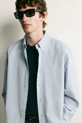 Camisa de corte regular fit confeccionada en algodón, con estampado de cuadros pequeños en tonos celestes. Presenta cuello abotonado, cierre frontal con botones y mangas largas con puños abotonados.