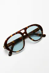 Lentes de sol con armazón negro de diseño envolvente y estilo aviador, con micas oscuras.