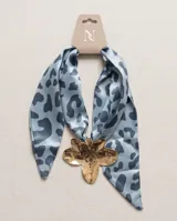 Pañuelo de seda celeste con estampado animal print azul y un dije metálico dorado en forma de flor que sujeta la prenda.
