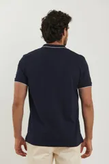 Chomba azul marino de piqué con cuello clásico y tapeta de dos botones. Detalles de ribete blanco en cuello y mangas.