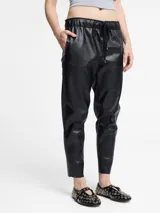 Pantalón de cuerina color negro con cintura elástica y cordón de ajuste. Presenta un corte tipo jogger con bolsillos laterales.