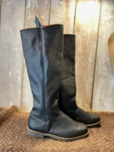 Botas de jinete de caña alta, confeccionadas en cuero negro con suela de goma resistente. Presentan un diseño clásico de equitación con costuras reforzadas y el logo grabado en el lateral.