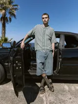 Polo de punto verde con rayas verticales blancas, corte relajado, cuello tipo camisa, cierre con botones y mangas cortas.