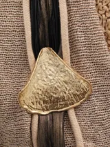 Collar dorado con colgante circular con diseño abstracto y textura labrada. El collar es de cordón negro.