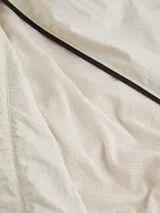 Campera Calvin Klein color beige claro, confeccionada en nailon arrugado reciclado. Tiene cuello alto, puños y bajo elásticos, cierre con cremallera, bolsillos con cremallera en la cintura, abertura de ventilación en la espalda, forro de poliéster reciclado e insignia con el logo de goma de Calvin Klein en la manga.