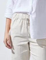 Pantalón de lino de corte recto y tiro medio, con pretina elástica ancha y lazo de ajuste frontal. Presenta bolsillos laterales verticales y bolsillos traseros.