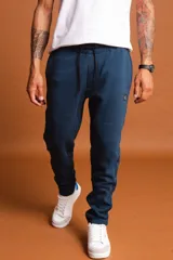 Pantalón de jogging azul piedra con cintura elástica ajustable mediante cordón, puños en los tobillos y etiqueta pequeña con logo en el lateral.