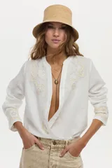 Camisa blanca de lino con cuello mao, manga larga y delicados bordados en tono tostado en el pecho y los puños.