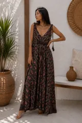Vestido largo sin mangas con escote en V y tirantes ajustables decorados con borlas colgantes. Presenta un estampado de diseño paisley en tonos oscuros y marrones, con falda amplia y fluida.