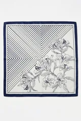 Pañuelo cuadrado con diseño dividido en dos secciones: una con estampado de líneas geométricas en zigzag y otra con ilustración botánica de flores tipo lirios. Presenta un borde perimetral en color azul oscuro.