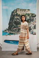 Vestido largo de tejido calado con rayas horizontales en tonos beige, marrón y amarillo. Tiene corte recto, hombros caídos, tajo lateral y logo bordado en la manga.