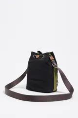 Bolso tipo bucket de Bimba y Lola, confeccionado en nylon negro con detalles en cuero color suela. Cuenta con cierre de cordón ajustable, bolsillo frontal con cierre y correa de hombro regulable de tejido.