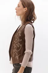 Chaleco marrón de simil cuero con bordado en color crema, cuello en V y cierre frontal con botones.