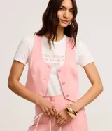 Remera de algodón blanca con cuello redondo y mangas cortas. Presenta una estampa frontal con la frase 'Too glam to give a damn' decorada con strass rosados y detalles de pliegues en los hombros.