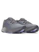 Championes de trail running Under Armour Charged Bandit TR 3, color gris con detalles en lila en la suela. Presentan una parte superior de malla técnica transpirable con refuerzos estratégicos, entresuela Charged Cushioning para mayor amortiguación y suela con tacos para tracción en terrenos irregulares.