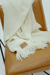 Ruana de lana merino color crudo, con textura tejida y terminaciones en flecos en los extremos. Incluye etiqueta de cuero con la marca Minetti.