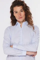 Camisa de tejido Oxford lisa y color blanco, con cuello camisero, cierre frontal de botones y mangas largas con puños abotonados.