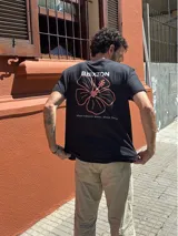 Remera negra de manga corta con estampado en la espalda de la marca Brixton y una flor de hibisco en color salmón, acompañada del texto 'Where hibiscus grows, peace flows'.
