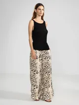 Top tejido sin mangas en punto canalé, color negro con hilos metálicos Lurex que le dan un brillo sutil. Presenta escote bote y un dije metálico en color oro rosado.