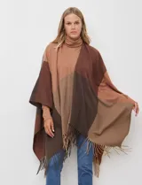 Ruana tejida con diseño colorblock en tonos de gris y beige, con flecos en el borde inferior.