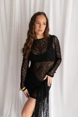 Vestido corto negro de encaje transparente, con mangas largas y falda ajustada con detalle lateral asimétrico tipo pareo.