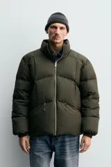 Cazadora acolchada de corte relajado confeccionada en tejido técnico color verde militar. Presenta cuello subido, cierre frontal con cremallera, mangas largas con puños elásticos y bolsillos frontales con cremallera oculta.