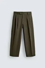 Pantalón relaxed fit color verde militar con pliegues frontales dobles, bolsillos delanteros y detalle de bolsillos traseros de vivo. Cierre frontal cruzado con cremallera y gancho metálico oculto.