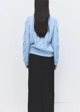 Sweater de punto celeste con diseño de trenzas en relieve, cuello redondo y mangas largas.