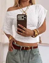 Top blanco de escote asimétrico con hombro descubierto, mangas cortas amplias y diseño entallado en el cuerpo con textura perforada tipo broderie.