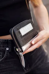Billetera chica de cuero negro con textura tipo cocodrilo y detalles plateados. Cuenta con cierre y logo de la marca en el frente.