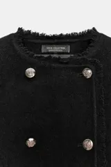 Chaqueta de corte recto confeccionada en mezcla de lana, con cuello redondo y manga larga. Presenta un diseño cruzado con botones metálicos plateados y acabados deshilachados en cuello, puños y ruedo.