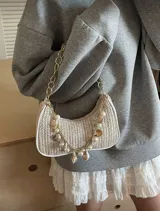 Cartera de mano color beige, tejida en rafia, con cadena dorada y apliques de dijes con forma de estrellas de mar, caracoles y perlas.