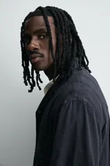 Camisa de algodón negro, de corte relajado (relax fit), con cuello bowling, manga corta y bolsillo plastrón en el pecho. Cierre frontal con botones a presión.