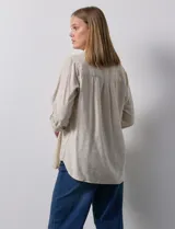 Camisa blanca de lino con cuello con solapa, manga larga regulable con presilla y botón, y abertura central con botones.