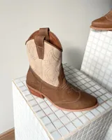 Botas estilo tejano de cuero vacuno en combinación de colores tostado y beige, con costuras decorativas en contraste y taco bajo de madera.
