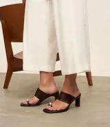 Sandalia tipo mule color marrón oscuro, con punta cuadrada, tacón alto y una tira ancha en el empeine. Presenta un detalle de dedera metálica plateada en la parte frontal.