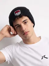 Gorro tipo beanie de punto acanalado en color negro, con parche bordado frontal que incluye el logo de la marca Rusty.