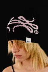 Beanie tejido reversible, con un lado negro y el otro lado rosado claro, ambos con diseño gráfico estampado en contraste.