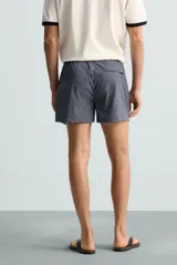 Bañador largo de hombre color rosa pálido con textura seersucker. Presenta cintura elástica ajustable con cordón blanco, bolsillos laterales y un bolsillo trasero de plastrón.