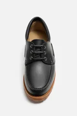 Zapato tipo náutico de cuero color marrón, con cordones, ojales metálicos laterales y suela de goma con volumen y relieve dentado.